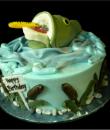 Fisherman's Birthday cake,  Green and blue buttercream iced,  round decorated with a large mouth bass, fishing lure, and cattails. Everything on this cake is EDIBLE.  (Serves 8-80 party slices)