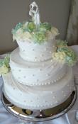 White buttercream iced,  3 tier round wedding cake decorated with pleated fondant ribbons, and pearls.  Fresh Hydrangea and white roses are used as the topper and cluster at the points. 
(This cake can serve receptions with 90-220 expected guests)
