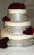 Candlelight buttercream iced,  3 tier round wedding cake decorated with Taupe Fondant ribbon and pearl dots in a champagne bubble pattern . Fresh Roses as the topper.  (This cake can serve receptions with 90-220 expected guests)